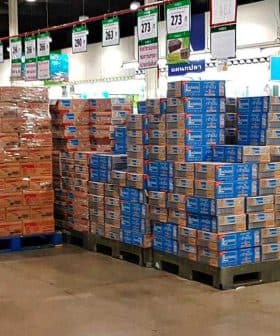 Pallets of stacked boxes in a retail store aisle with employees nearby. - Olive Oil Times