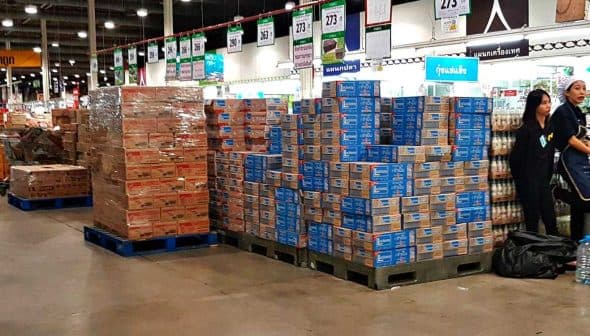 Pallets of stacked boxes in a retail store aisle with employees nearby. - Olive Oil Times