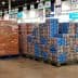 Pallets of stacked boxes in a retail store aisle with employees nearby. - Olive Oil Times
