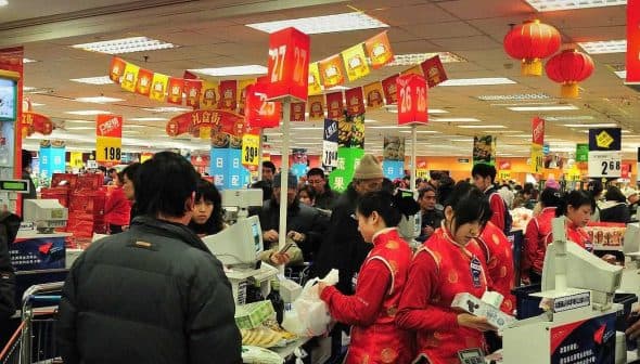 Crowd of shoppers and cashiers at a busy supermarket checkout area with red decorations. - Olive Oil Times