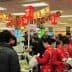 Crowd of shoppers and cashiers at a busy supermarket checkout area with red decorations. - Olive Oil Times