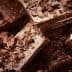 Pieces of dark chocolate stacked with chocolate shavings scattered around on a wooden surface. - Olive Oil Times
