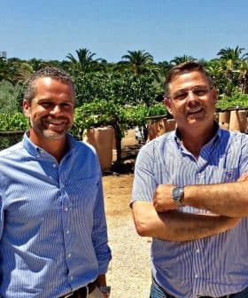 Two men standing in an olive grove, smiling and posing for the camera. - Olive Oil Times