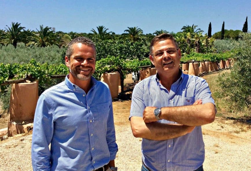 Two men standing in an olive grove, smiling and posing for the camera. - Olive Oil Times