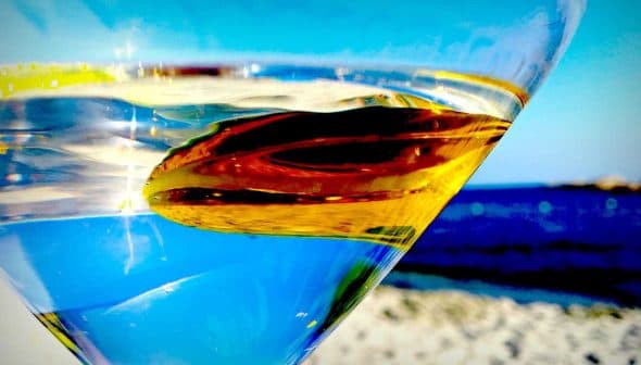 Close-up of a martini glass filled with clear liquid and an olive, with a blurred background. - Olive Oil Times