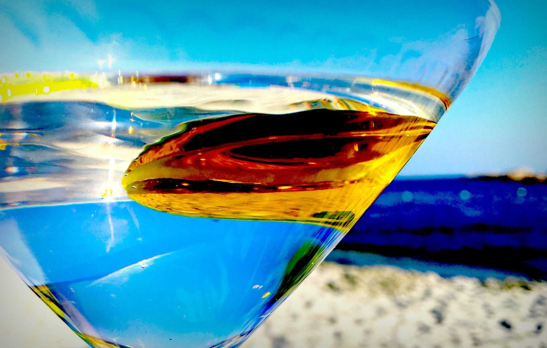 Close-up of a martini glass filled with clear liquid and an olive, with a blurred background. - Olive Oil Times