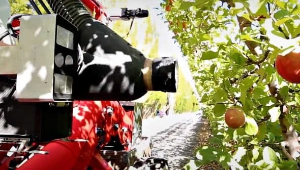 Close-up of a fruit harvesting machine positioned near apple trees in an orchard. - Olive Oil Times