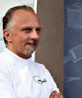 Chef wearing a white uniform standing in front of a sign for a culinary festival. - Olive Oil Times