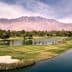 A panoramic view of a golf course featuring water hazards and palm trees with mountains in the background. - Olive Oil Times