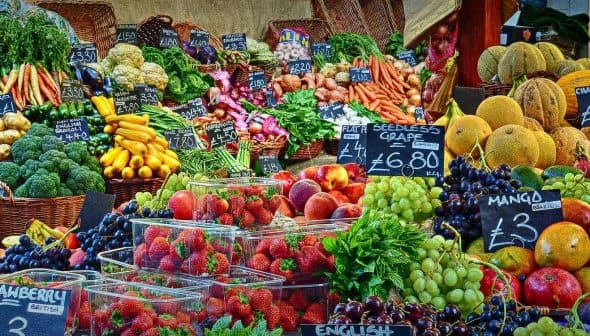 A vibrant assortment of fresh fruits and vegetables arranged at a market stall with price tags. - Olive Oil Times