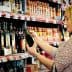 Woman inspecting a bottle of olive oil in a grocery store aisle filled with various products. - Olive Oil Times