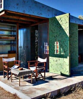 A modern outdoor structure with green walls and two wooden chairs in front of it. - Olive Oil Times