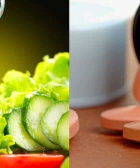 Olive oil being poured over a fresh salad with cucumber and tomato alongside statin tablets on a wooden surface. - Olive Oil Times