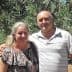 A couple standing together in an olive grove, smiling at the camera. - Olive Oil Times