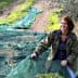 Woman gathering olives on a green tarp in an olive grove during harvest season. - Olive Oil Times