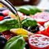 Fresh salad with tomatoes, mozzarella, olives, and basil being drizzled with olive oil. - Olive Oil Times