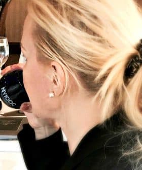 A woman with blonde hair tied in a ponytail holding a blue cup while seated at a table. - Olive Oil Times