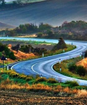 A winding road through a rural landscape with hills and vegetation on either side. - Olive Oil Times