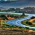 A winding road through a rural landscape with hills and vegetation on either side. - Olive Oil Times