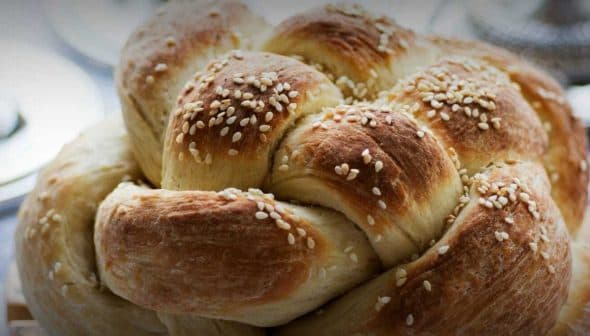 A round loaf of challah bread topped with sesame seeds, showcasing a braided design. - Olive Oil Times