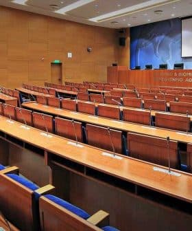 Interior view of a conference room featuring wooden seating and a presentation screen. - Olive Oil Times