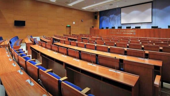 Interior view of a conference room featuring wooden seating and a presentation screen. - Olive Oil Times