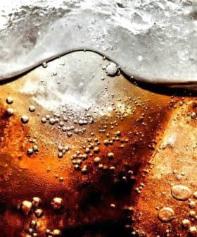 Close-up image of a carbonated beverage with ice cubes and bubbles visible in the liquid. - Olive Oil Times