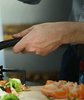 A person stirring food in a frying pan while preparing ingredients on a kitchen countertop. - Olive Oil Times