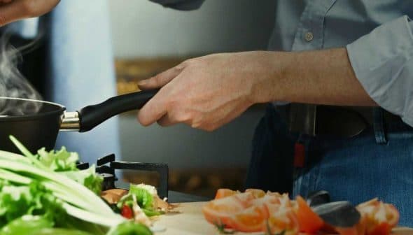 A person stirring food in a frying pan while preparing ingredients on a kitchen countertop. - Olive Oil Times