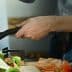 A person stirring food in a frying pan while preparing ingredients on a kitchen countertop. - Olive Oil Times