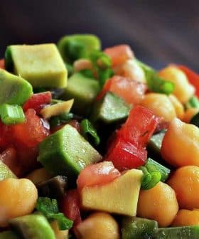 A close-up of a chickpea salad with diced avocado, tomatoes, and green onions in a white bowl. - Olive Oil Times