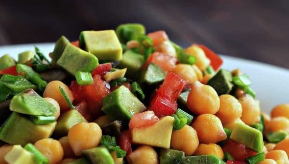 A close-up of a chickpea salad with diced avocado, tomatoes, and green onions in a white bowl. - Olive Oil Times