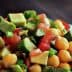A close-up of a chickpea salad with diced avocado, tomatoes, and green onions in a white bowl. - Olive Oil Times