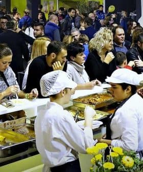 Crowd of people enjoying food at a culinary event with chefs serving dishes. - Olive Oil Times