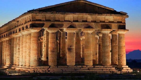 Ancient Greek temple structure with tall columns illuminated at dusk in Paestum, Italy. - Olive Oil Times