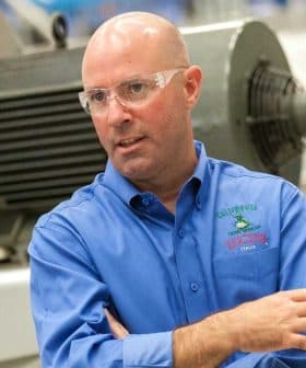 Man wearing a blue shirt and safety glasses, gesturing while speaking in an industrial setting. - Olive Oil Times