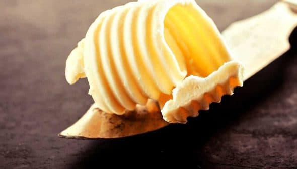 A portion of butter shaped in ridges resting on a metal butter knife. - Olive Oil Times