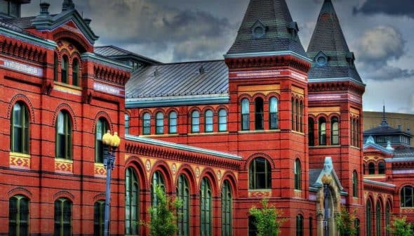 Historic red brick building featuring multiple towers and arched windows against a cloudy sky. - Olive Oil Times
