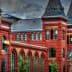 Historic red brick building featuring multiple towers and arched windows against a cloudy sky. - Olive Oil Times