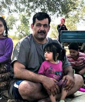 A family sitting together during a break from harvesting, with children and adults in casual clothing. - Olive Oil Times