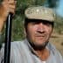 A man wearing a cap and glasses, holding a stick while standing in an olive grove. - Olive Oil Times