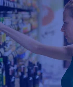 Woman reaching for a bottle of olive oil on a supermarket shelf filled with various oils. - Olive Oil Times