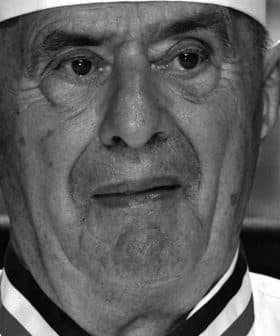 Black and white portrait of an elderly chef wearing a white uniform and hat. - Olive Oil Times