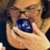 Woman with glasses smelling olive oil from a blue tasting cup while holding a small container. - Olive Oil Times