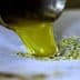 Stream of green olive oil pouring from a metal spout onto a surface. - Olive Oil Times