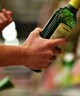 A person holding a green bottle of olive oil while shopping in a grocery store aisle. - Olive Oil Times