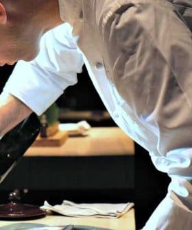 Chef in a white uniform carefully plating a dish with a sauce from a bottle. - Olive Oil Times