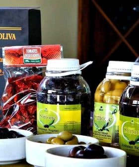 Bottles of olive oil, olives, and other products from Olivicola Simone displayed on a table. - Olive Oil Times
