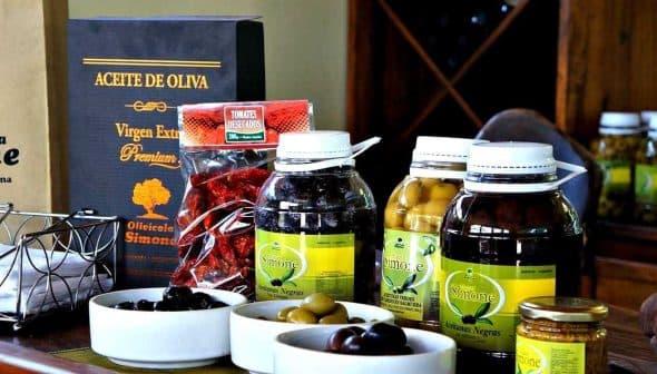 Bottles of olive oil, olives, and other products from Olivicola Simone displayed on a table. - Olive Oil Times