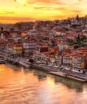 A panoramic view of Porto's riverfront at sunset with colorful buildings along the water's edge. - Olive Oil Times